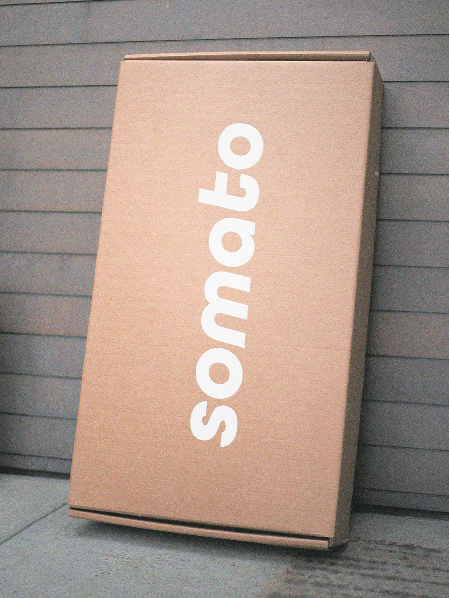 Compact boxed Somato Reformer delivered to a home, leaning upright by the front entrance.