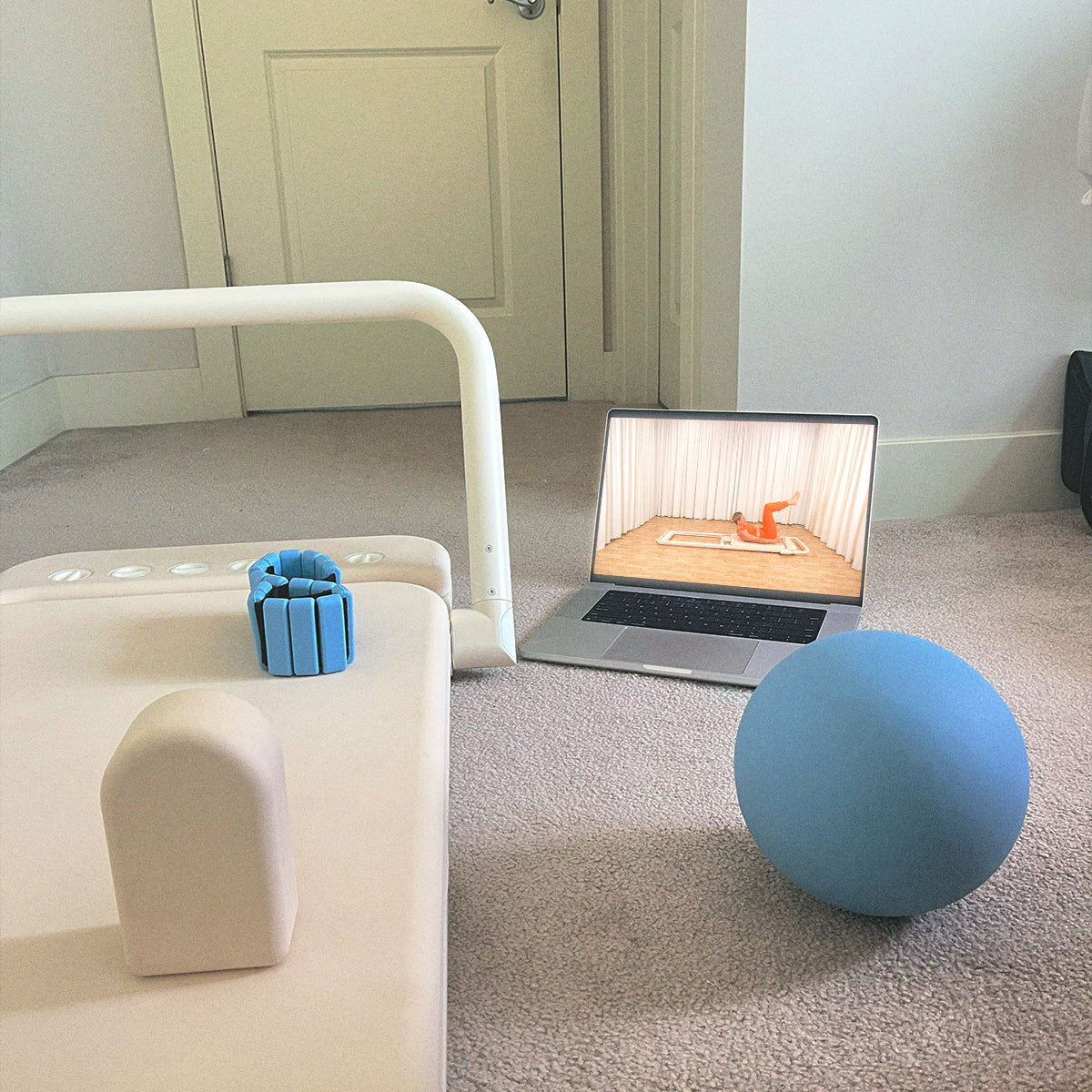 Somato Reformer positioned for an at-home workout with a Pilates class playing on a laptop.