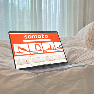 Somato app home screen open on a laptop resting on a bed, ready for a Pilates workout.
