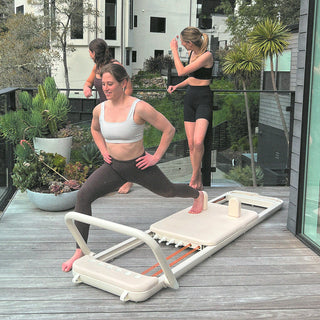At-home Pilates session with one woman on the Somato Reformer and two friends socializing nearby.